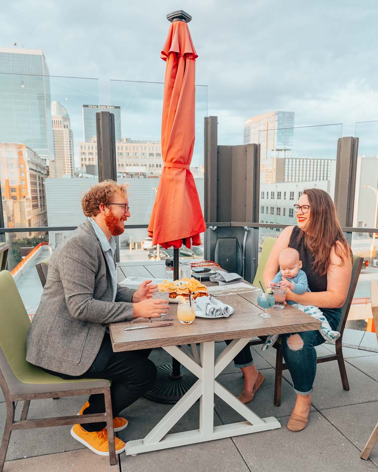 Lia and Jeremy Garcia with baby on a rooftop restaurant overlooking Louisville, Kentucky