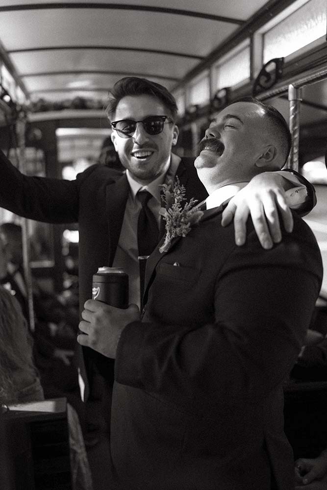 Black and white photo of groomsmen laughing in a trolley during a wedding shuttle